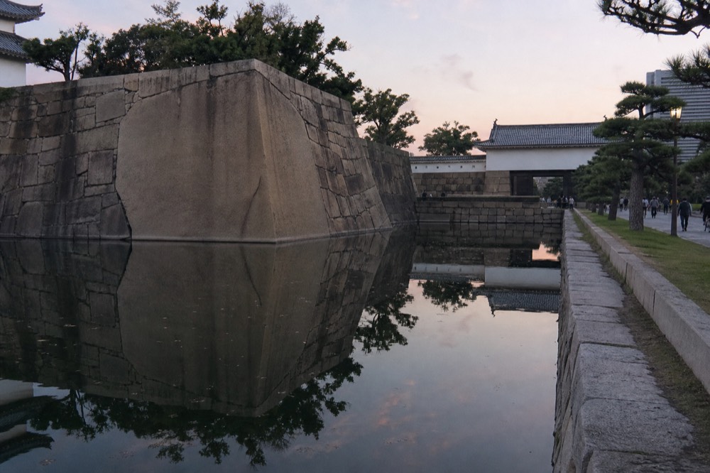 A stone rampart of massive fitted blocks reflected in a still moat at dusk