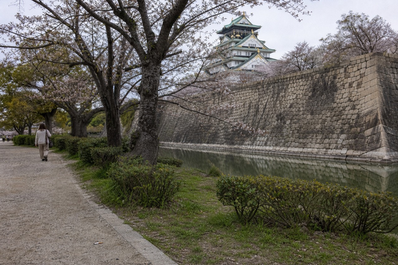 A stone wall of large fitted granite blocks beside a moat, with a white castle tower rising behind trees