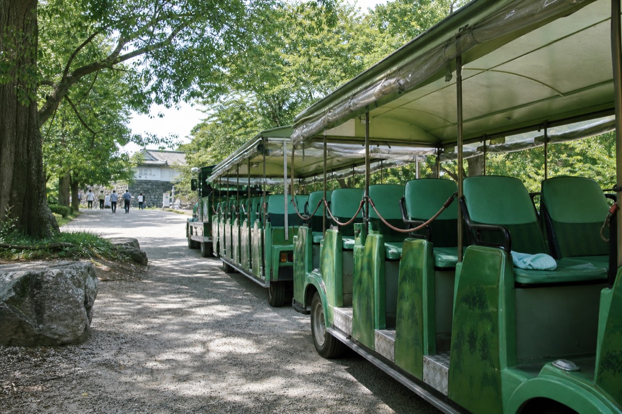 A green Road Train shuttle car passing in front of the stone walls of Osaka Castle