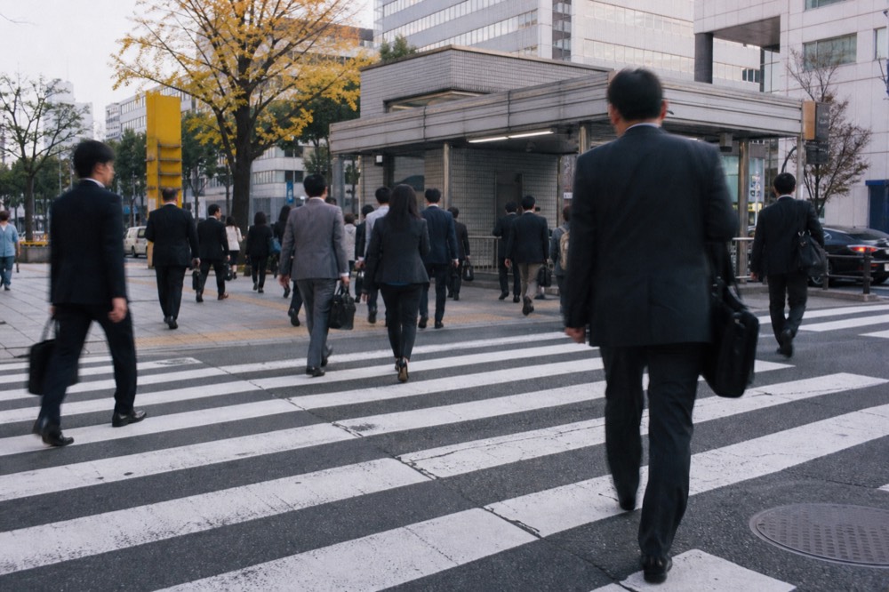 Commuters crossing a wide street in central Osaka on a weekday morning
