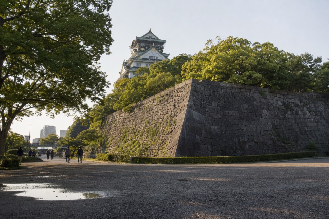 White Osaka Castle keep rising above stone walls and green trees