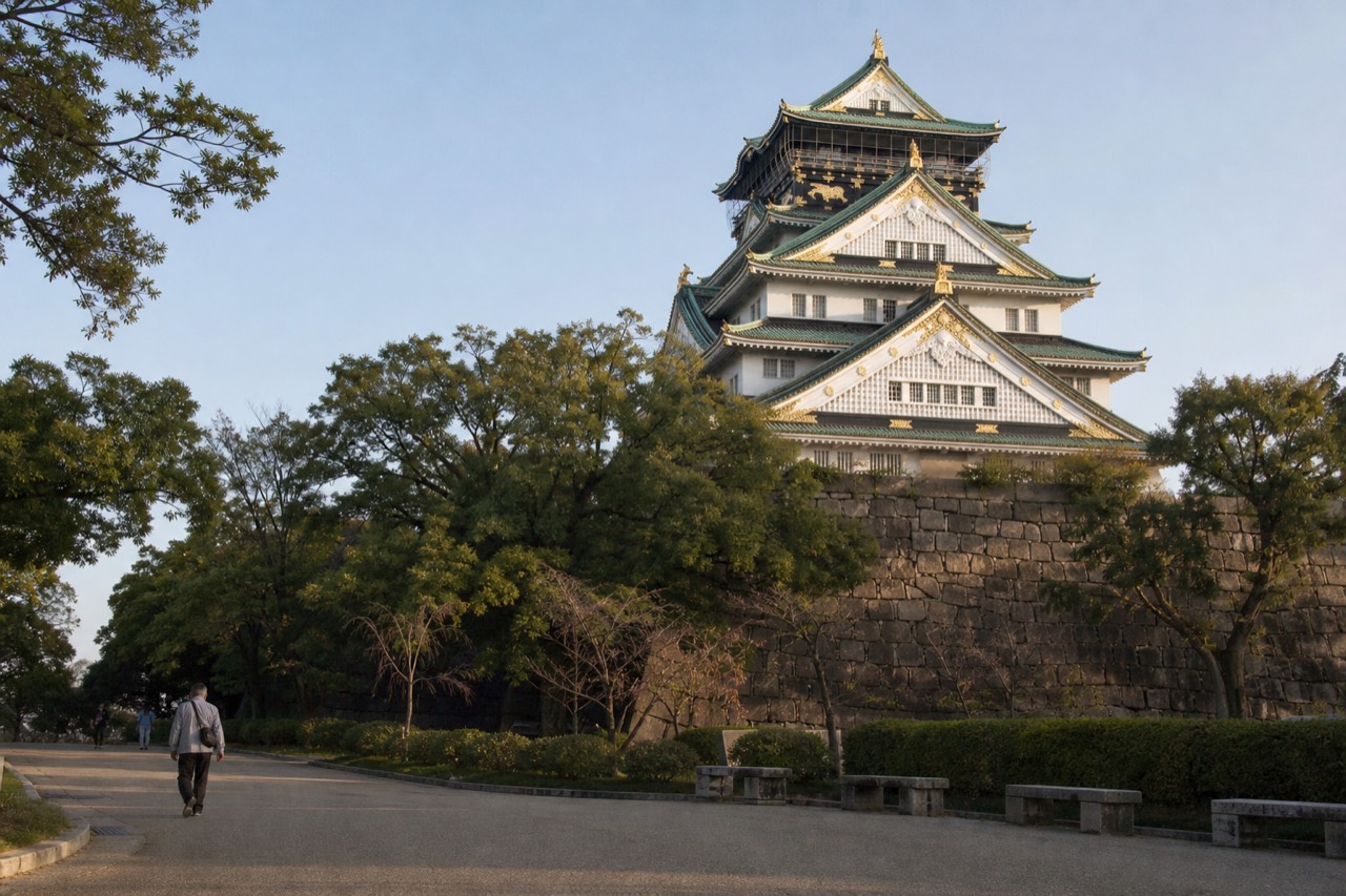 White Osaka Castle tower rising above stone walls and green trees