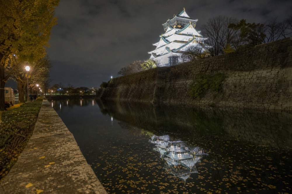 The floodlit white tower of Osaka Castle reflected in the inner moat at night