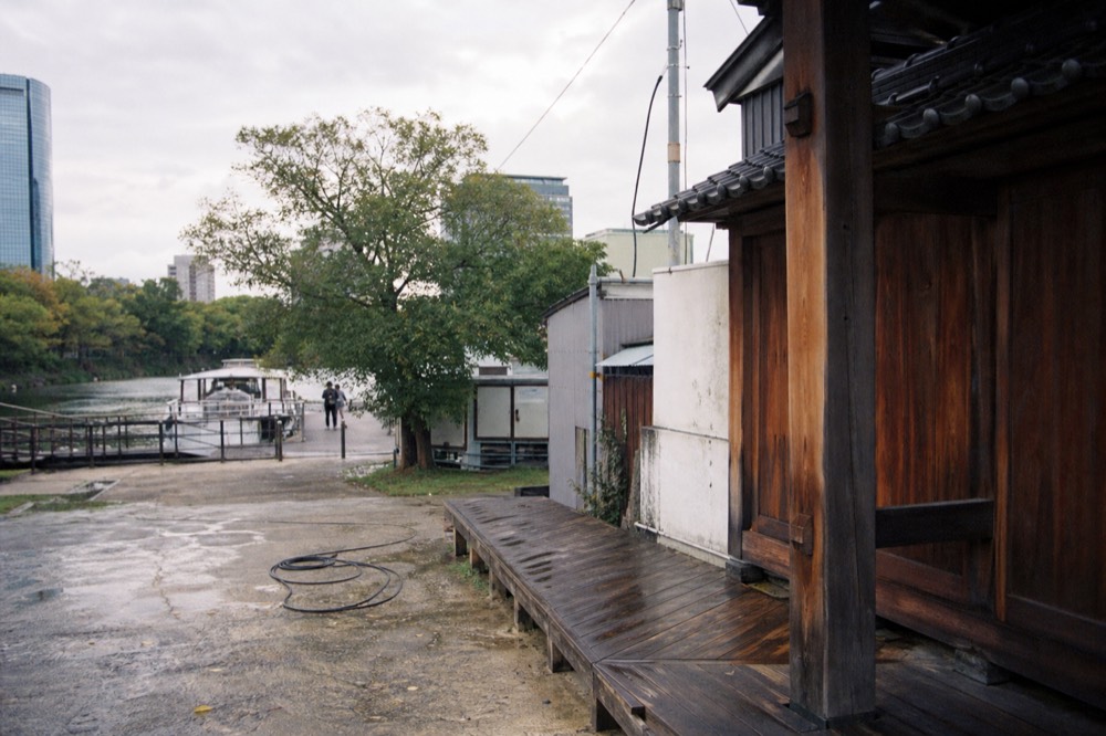 A wooden film-set castle gate standing on a waterfront lot beside weathered industrial buildings