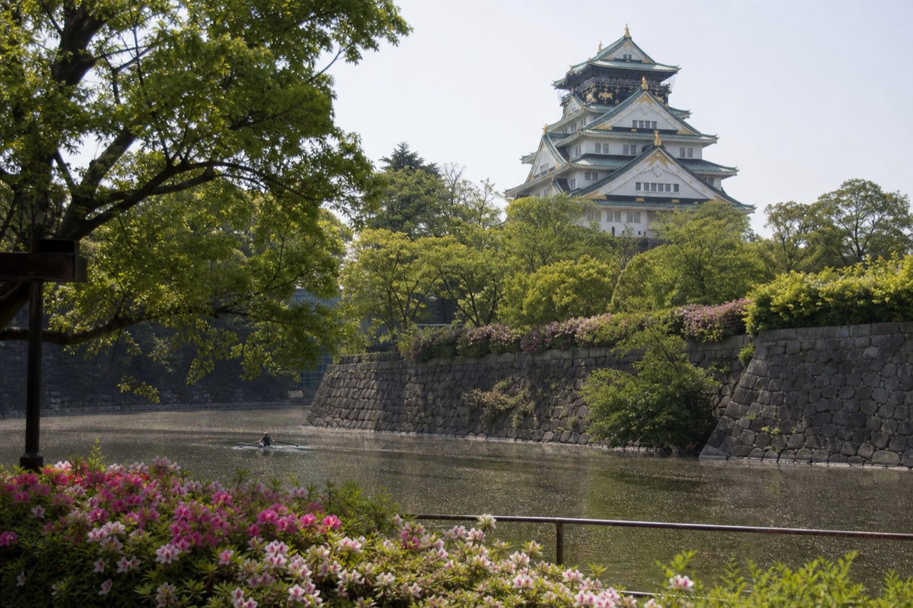 Osaka Castle tower rising above moat and green park trees under a clear sky