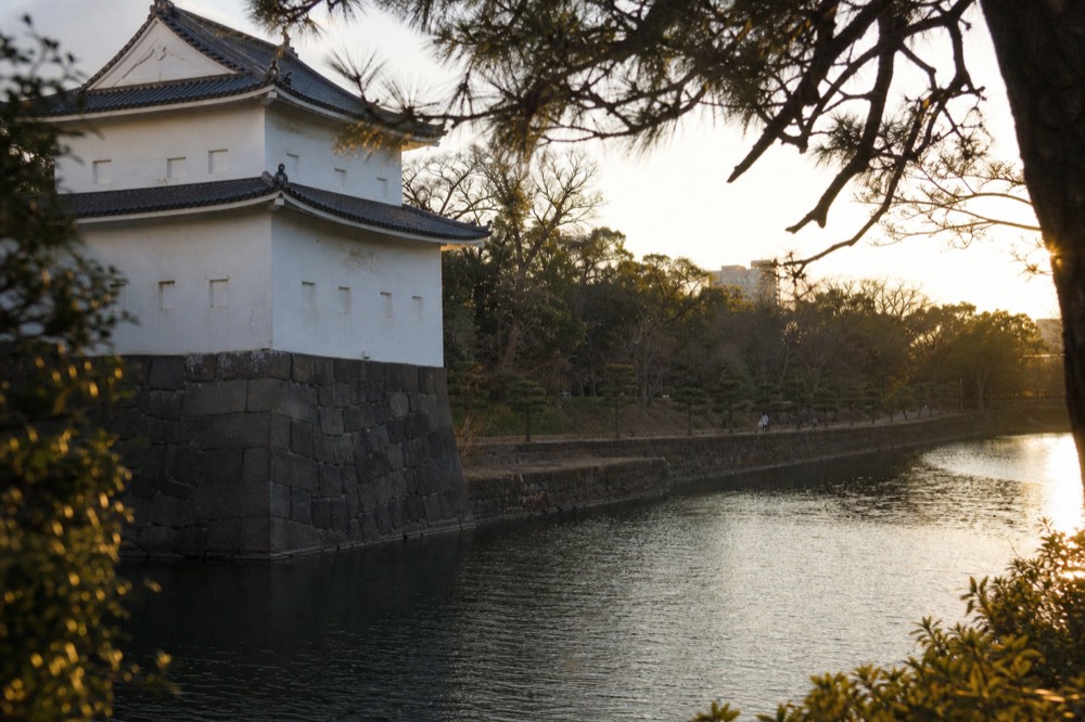 White plaster turret building with green copper roof beside a moat