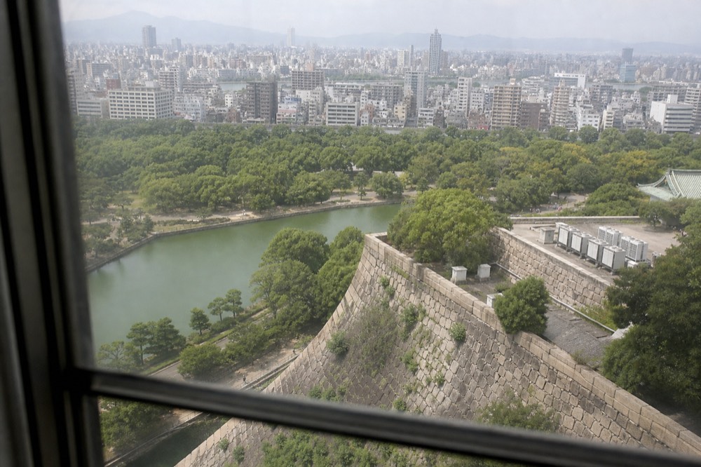 View across Osaka rooftops and green parkland from a high vantage point with moat curving below