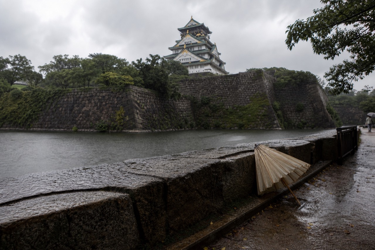 Rain clouds over Osaka Castle tower and the outer moat, with wet stone walls in the foreground