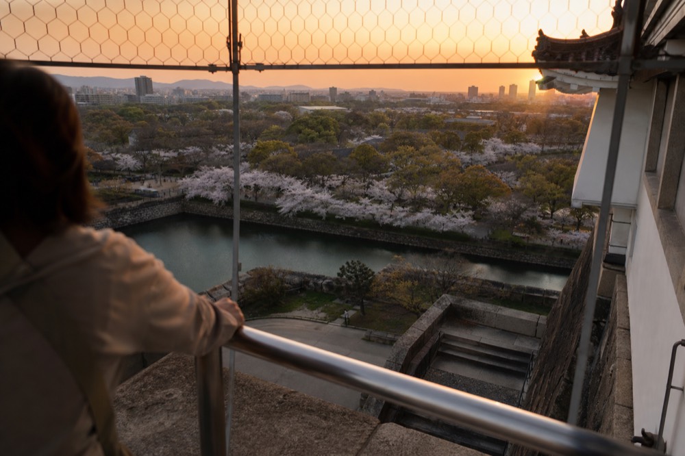 Tokyo-style skyscraper panorama from a tall glass observation deck at sunset with distant mountains