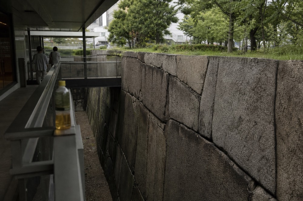 A stretch of massive grey stone wall below the Osaka Castle tower, with moat water in the foreground
