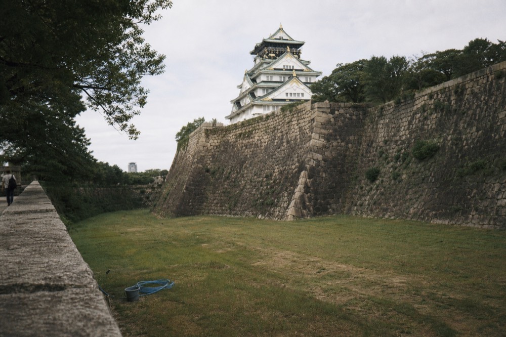 The Osaka Castle tower seen across a wide stone wall and dry moat in daylight