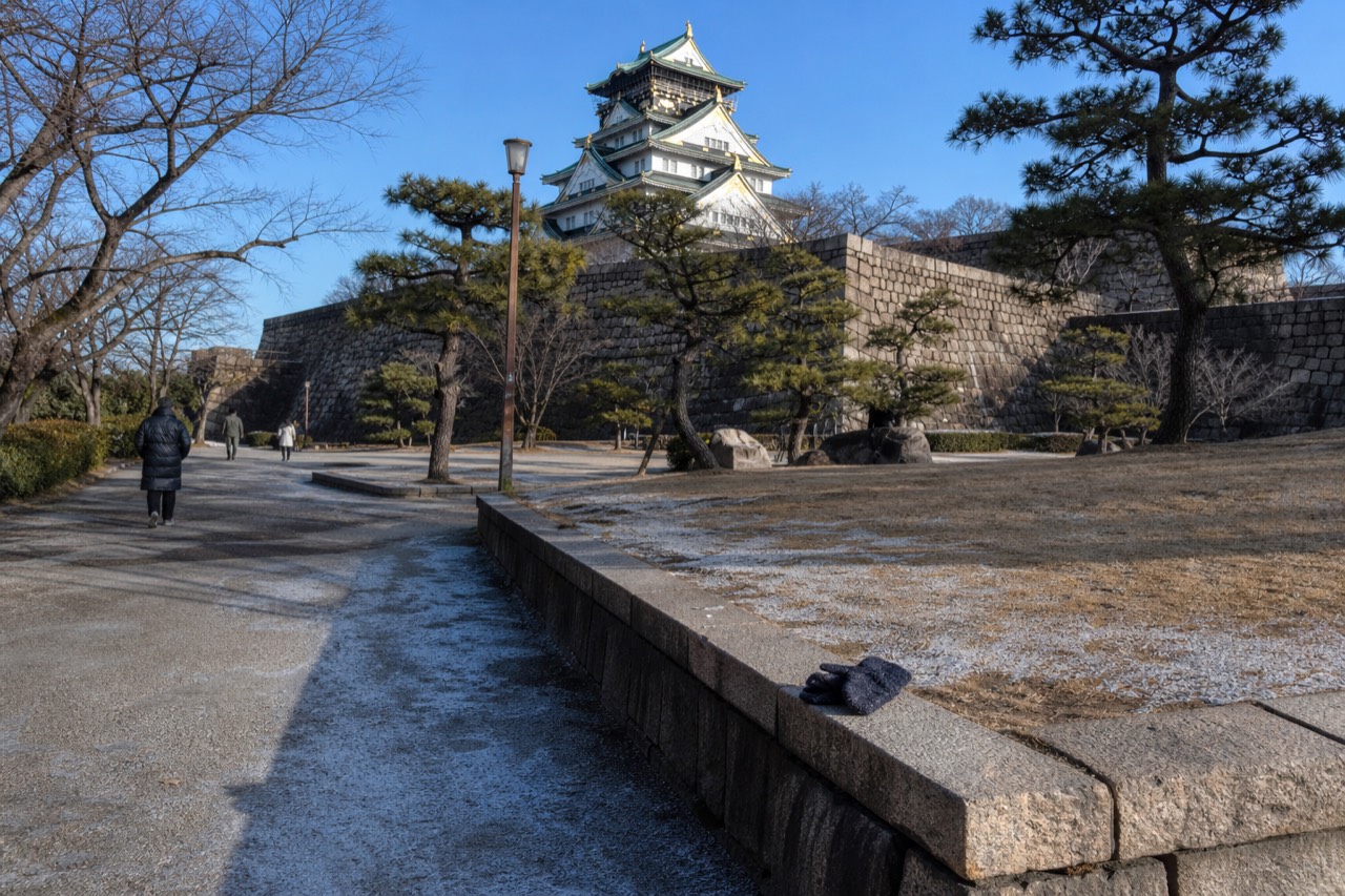 The white Osaka Castle Main Tower rising above stone walls and green trees in the park
