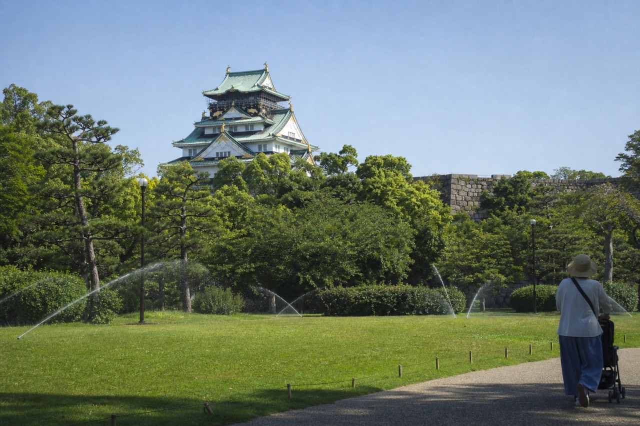 Osaka Castle tower rising above stone walls and green trees under a clear sky