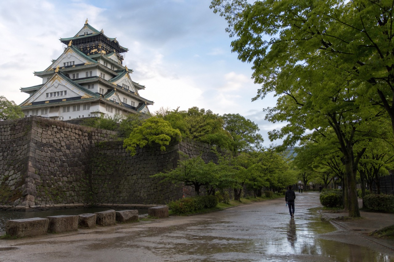 White Osaka Castle tower rising above stone walls and green trees under a clear sky