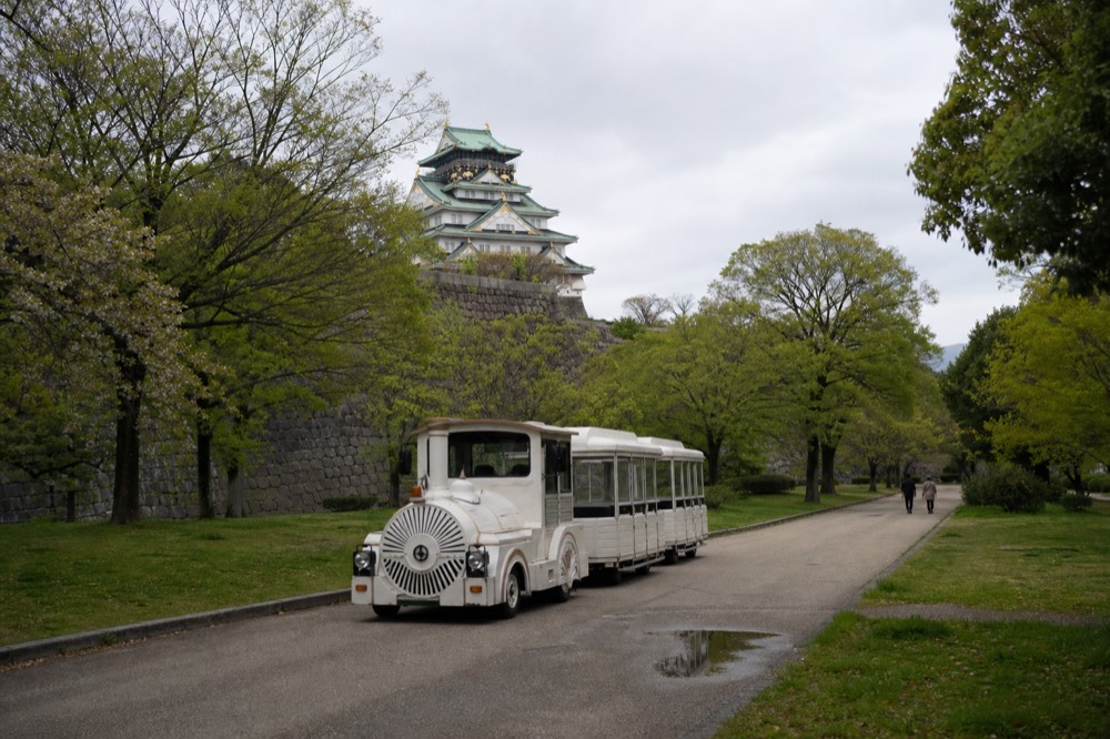 The Tamatsukuri-guchi gate area with the road train track and a sign pointing to the castle, surrounded by greenery