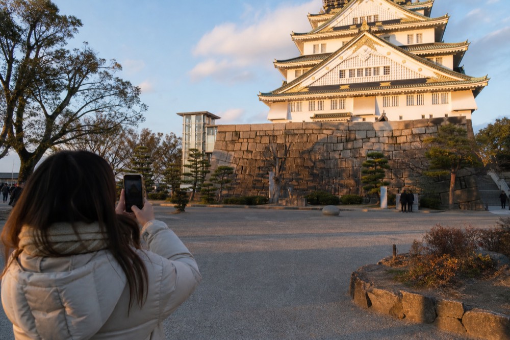 A visitor photographing the castle facade from the Honmaru plaza