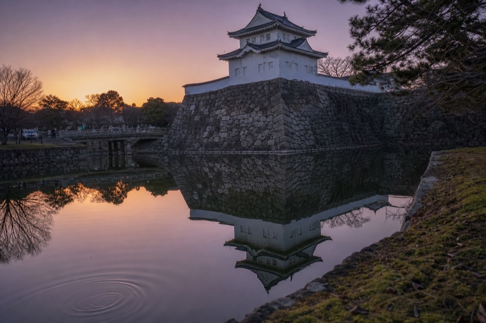 Osaka Castle tower and white walls reflected in the still water of the inner moat at dusk