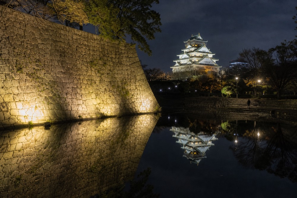 The floodlit tower reflected in the inner moat, with the stone walls of the honmaru lit from below