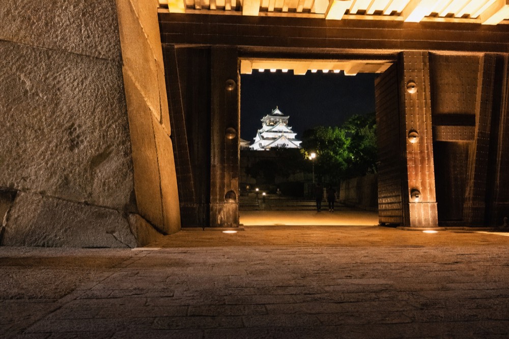 The Sakura-mon gate lit at night, with the stone walls and the tower visible in the background
