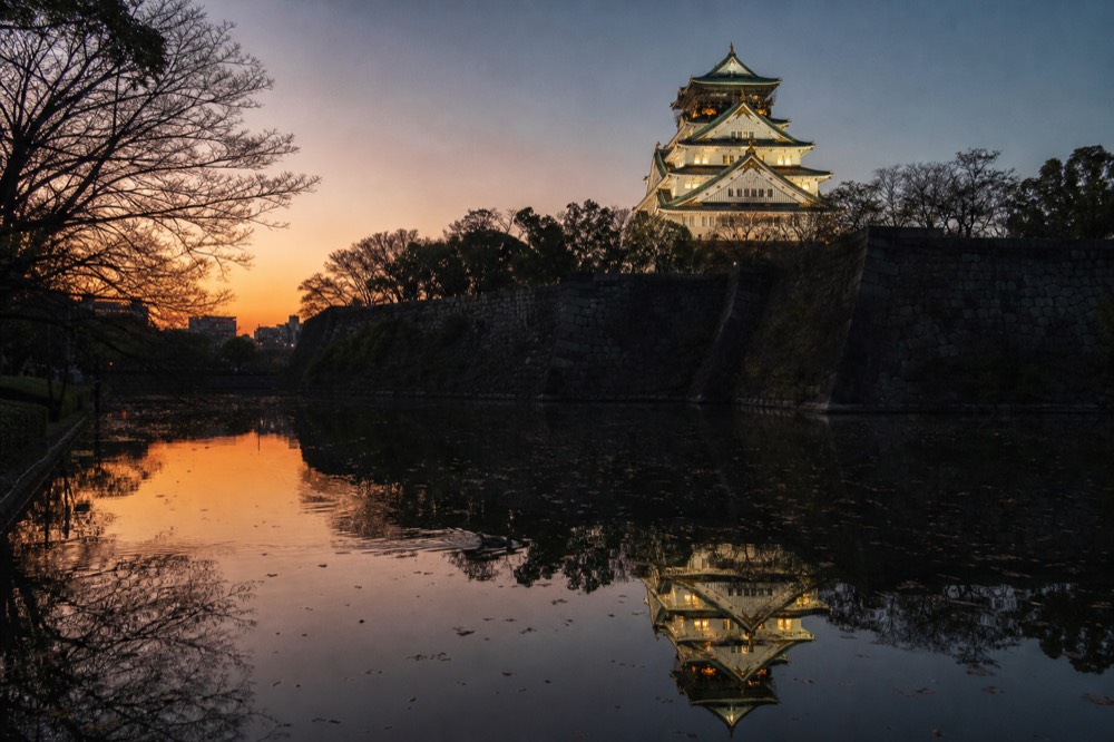 The castle's reflection in the inner moat at dusk, with the sky turning from orange to deep blue behind the floodlit tower