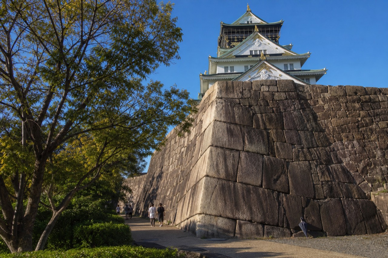 Gold and black Osaka Castle tower rising above a stone wall base under a clear sky
