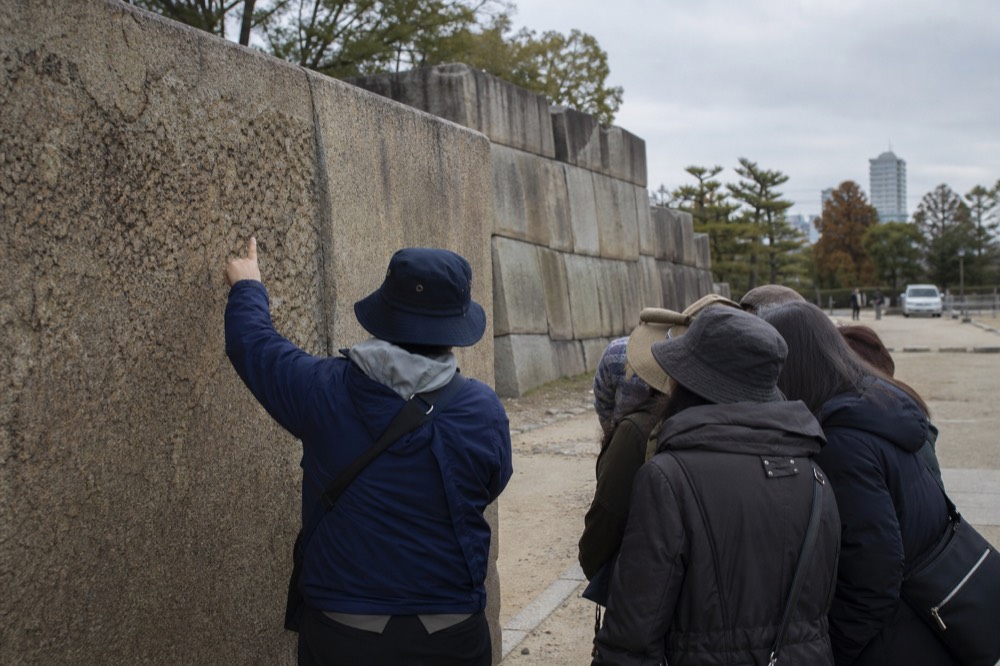A guide pointing to a detail on the castle's stone wall while a small group listens.