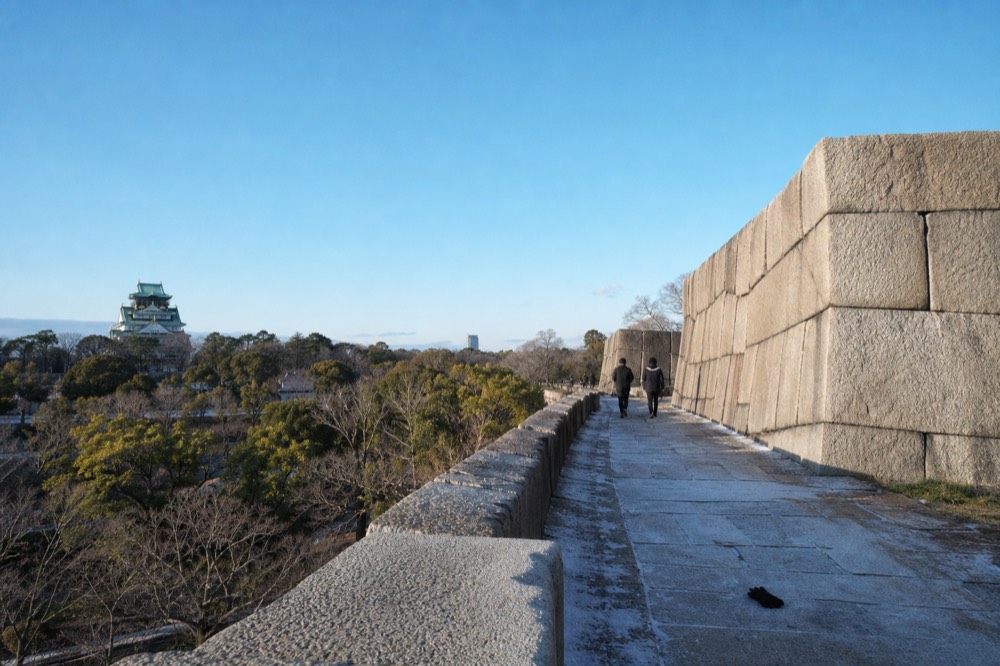 The stone walls of Osaka Castle with the tower in the distance under a clear sky.