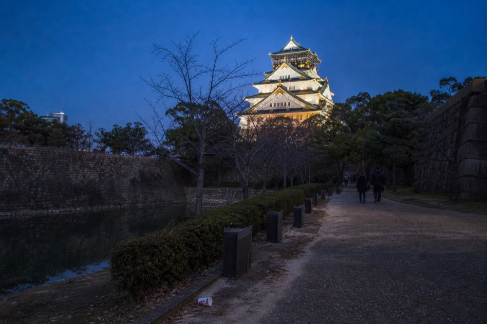The main tower of Osaka Castle lit up at dusk with the park in the foreground.