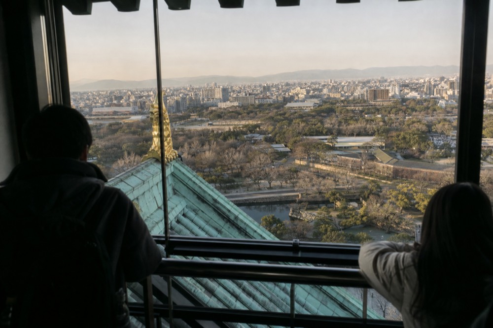 The interior of Osaka Castle's 8F observation deck with visitors looking out at the city