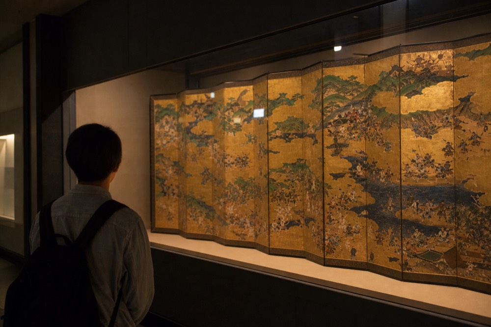 A historical Japanese folding screen painting displayed in a darkened gallery case