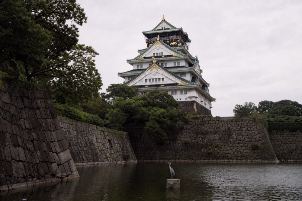 A white castle keep with layered green copper roofs seen across a moat
