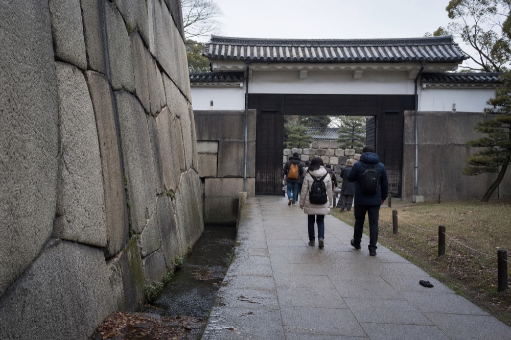Visitors walking on a stone path beside a moat toward a castle gate