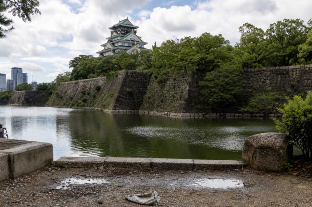 Wide view across the outer moat toward Osaka Castle with stone walls and green trees