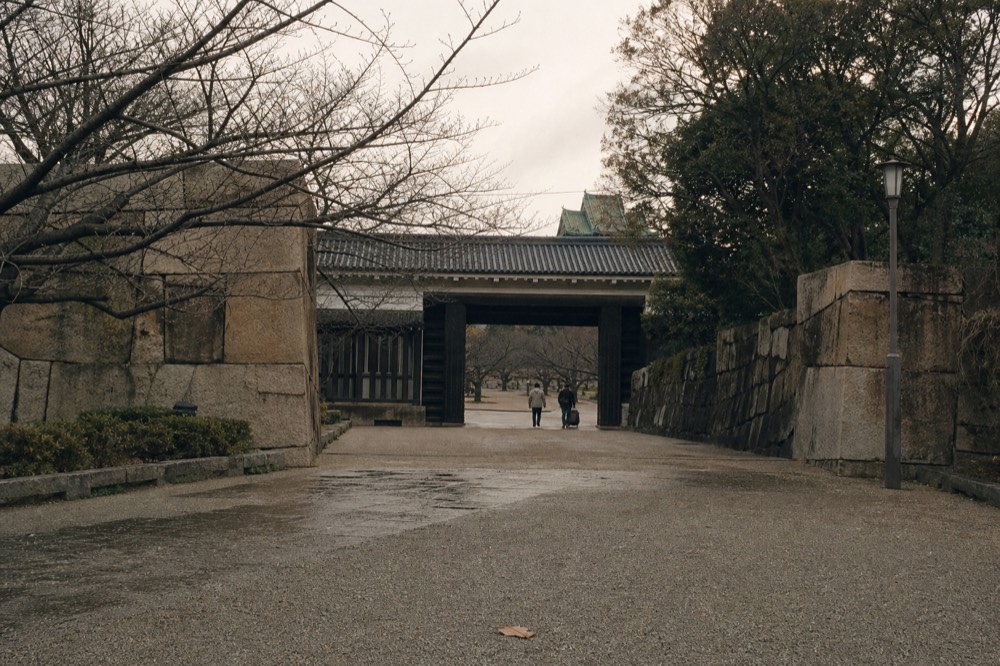 Stone gate of a castle entrance framed by trees with empty approach path