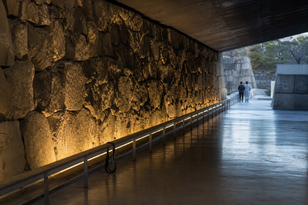 Underground exhibition hall with a long stretch of old stone wall lit along its base